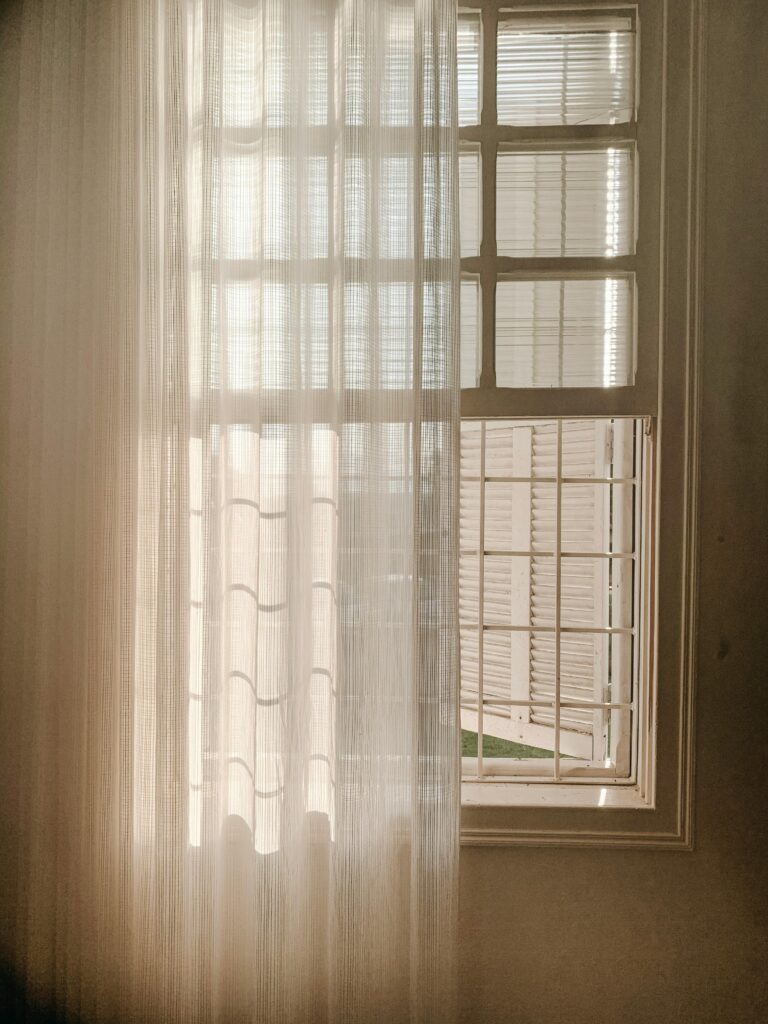 pexels-photo-3255244-3255244 A serene view of sunlight filtering through sheer window curtains, casting soft shadows indoors.
